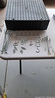 Stack of black peg board squares with various metal hooks and accessories laid out on table.
