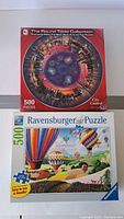 Shot of two puzzle boxes stacked, showing The Round Table Collection City Central 500-piece puzzle on top and Ravensburger hot air balloons puzzle underneath.
