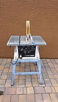 Front view of Kilsaw table saw on blue metal stand with yellow blade guard and power cord.