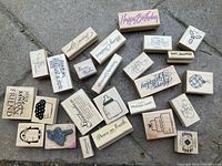Photo showing an overhead view of approximately 25 wooden stamps spread out on a surface, displaying various text and image designs related to holidays, celebrations, and kindness messages.