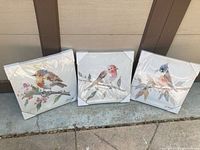 Three bird print artworks still in original plastic packaging with corner protectors, showing three different bird designs on branches with leaves.