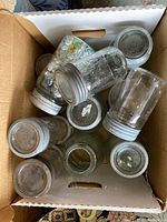 Top view of a box containing a mix of about a dozen vintage canning jars with metal lids, some jars tilted and some dust or residue on lids.