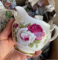 Close-up of creamer jug with large pink and white rose floral design and gold accents.