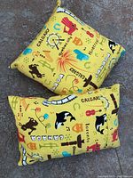 Two Canada themed decorative pillows, one square and one rectangular, featuring colorful graphics and city names on yellow fabric.