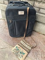 Front view of small black carry-on suitcase with handbag hanging in front