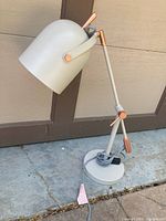 Photo of an adjustable gray desk lamp with bronze accents, showing entire lamp on concrete ground in front of a building wall.