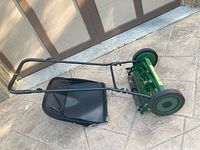 Side view of the whole push mower showing the green metal reel mower with two wheels and black grass catcher bag.