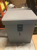 Front view of closed grey metal lock box showing CleverMade brand and front lock with key.