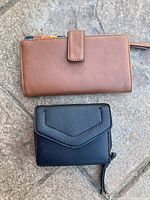 Top view of two Mia & Luca wallets; one black smaller wallet and one larger brown wallet on a stone surface.
