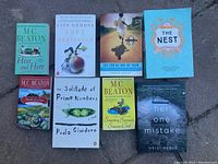 Eight paperback novels arranged in two rows on a stone surface, showing titles and authors clearly.