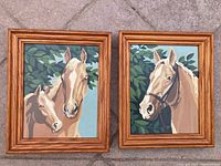 Photo of two vintage framed paint by numbers horse paintings side by side showing wooden frames and leafy backgrounds in excellent shape.