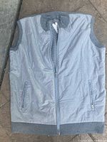 Front view of a light gray sleeveless vest jacket with a full front zipper, zippered hand pockets, ribbed collar and armholes