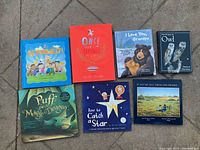 Photo showing seven children's books arranged on floor with colorful covers depicting various themes such as self-expression, alphabet, family love, fantasy, nature, and prairie life.