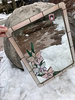 Full view of the rectangular stained glass mirror resting against a rock outdoors with visible cracked top left corner.