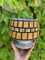 Front view of the mustard yellow and brown/black West German planter pot with geometric rectangular block pattern and gray marbled base and pedestal.