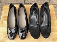 Front view of two pairs of women's shoes placed side by side. Franco Sarto black suede peep-toe heels on the right and Ara black patent crocodile pattern shoes on the left.