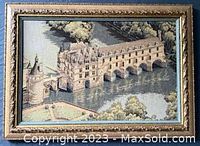 Framed needlepoint artwork showing an aquaduct and surrounding landscape.