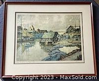 Framed mountain and coastal village art print with signature and muted color scheme.