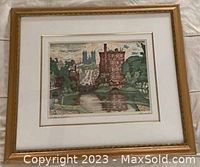 Image of the framed print showing a summer scene of Guelph featuring a brick tower, reflective water, green trees, and a distant cathedral with the artist's signature visible bottom right.
