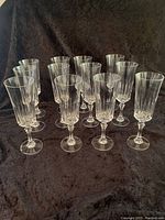 Twelve crystal champagne flutes arranged in rows on a dark textured surface showing their design, height, and shape.