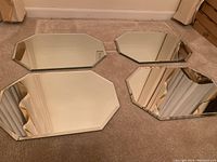 Set of four beveled mirror placemats shown laid on carpet floor, octagonal shape visible with beveled edges and clear reflective surface.