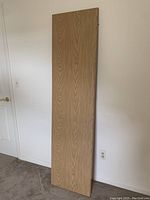 Full view of rectangular wooden desk top board leaning against wall showing overall size and shape.