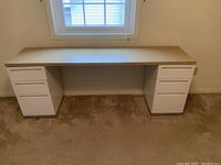 Front view of laminate desktop top spanning two white rolling file cabinets under a window.