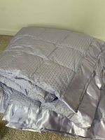 Folded lilac down comforter showing quilted square pattern and satin border trim