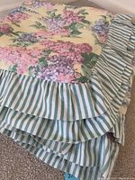 Close-up view showing floral pattern with ruffled striped edging of the bedspread.