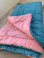 Full view of the reversible comforter laid out, showing teal green side and salmon pink side partially flipped over.