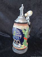 Front and side view of the limited edition Galileo Millennium beer stein showing embossed years 1995-1999 and the figure of Galileo on top of the pewter lid next to a golden spinning globe on the handle.