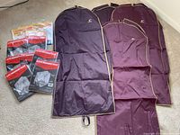 Four maroon fabric garment bags with zipper closures and 'JC' initials, arranged vertically on the floor.