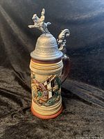 Full front left view of the lidded beer stein showing embossed colorful design and mounted soldier lid figure.