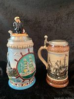 Both German beer steins together showing full designs and finials