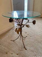 Full front-angle view of round glass top table with ornate gold-tone metal base designed to resemble long stem roses with leaves and buds.