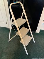 Front view of the three-step metal ladder standing upright showing white frame and grey steps.