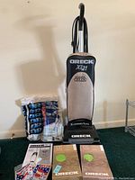 Oreck XL21 HEPA CELOC upright vacuum standing with extra vacuum bags and replacement filters placed in front and beside it