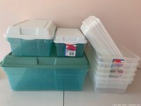 Photo showing large, medium, and small translucent green plastic bins with white and gray lids alongside the five clear plastic bins with white lids.