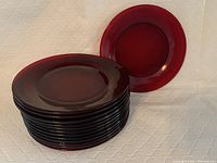 Stack of 13 deep ruby red cranberry glass plates with smooth rounded edges.