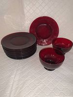 Photo showing stacked ruby red cranberry glass plates and two matching bowls against a white textured background.