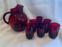 Photo showing the full set of ruby red glass pitcher and six matching drinking glasses on display against a white background.