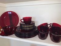 Full view of stacked ruby red plates, cups, and saucers on shelf.
