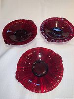 Top view of three ruby red glass canapé platters arranged on white tablecloth showing scalloped edges and handles.