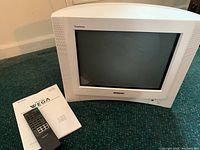 Front view of white Sony Trinitron Wega CRT TV with remote control and instruction manual placed in front