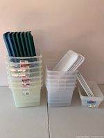 Stacks of translucent plastic storage bins with blue and green lids placed vertically in the bins.