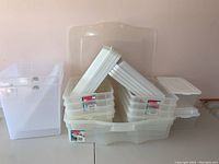 Group of clear plastic storage bins stacked with lids, some Rubbermaid labeled.