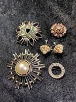 Top down view showing all jewelry pieces including brooches and earrings on dark fabric.