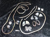 Full lot of vintage sterling silver jewelry displayed on black background showing various earrings, necklaces, bracelets and a bow brooch.