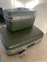 Photo showing stacked olive green vintage American Tourister luggage with textured hard shell and silver metal locks.