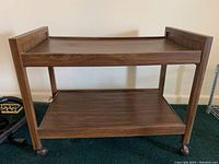 Full side view of vintage wooden cart with two shelves and caster wheels.